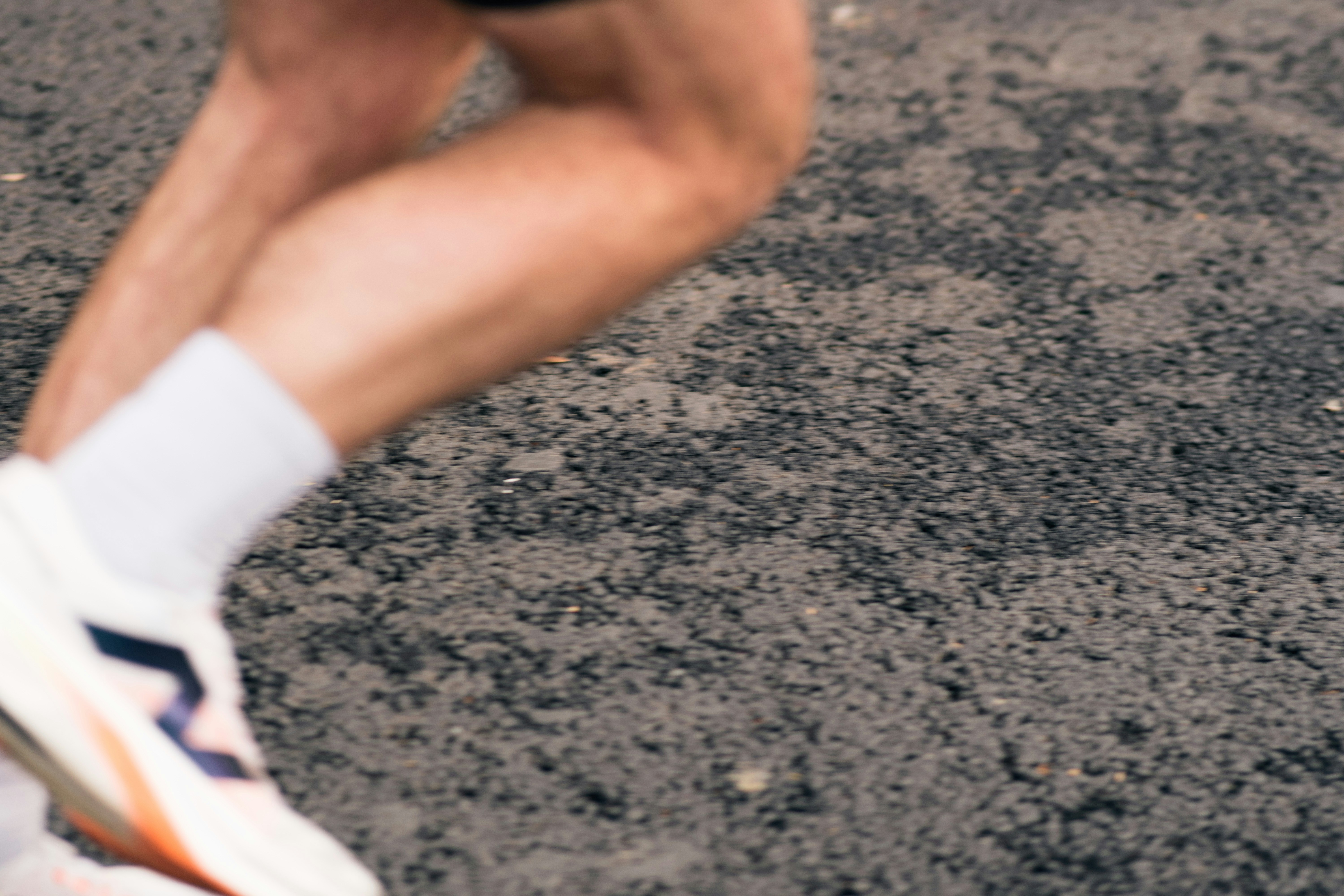 A closeup of two muscular legs wearing white socks and running sneakers in action, running on grey pavement.